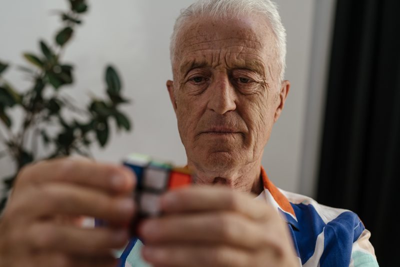 Elderly man concentrating on solving a Rubik's Cube, showing focus and mental agility